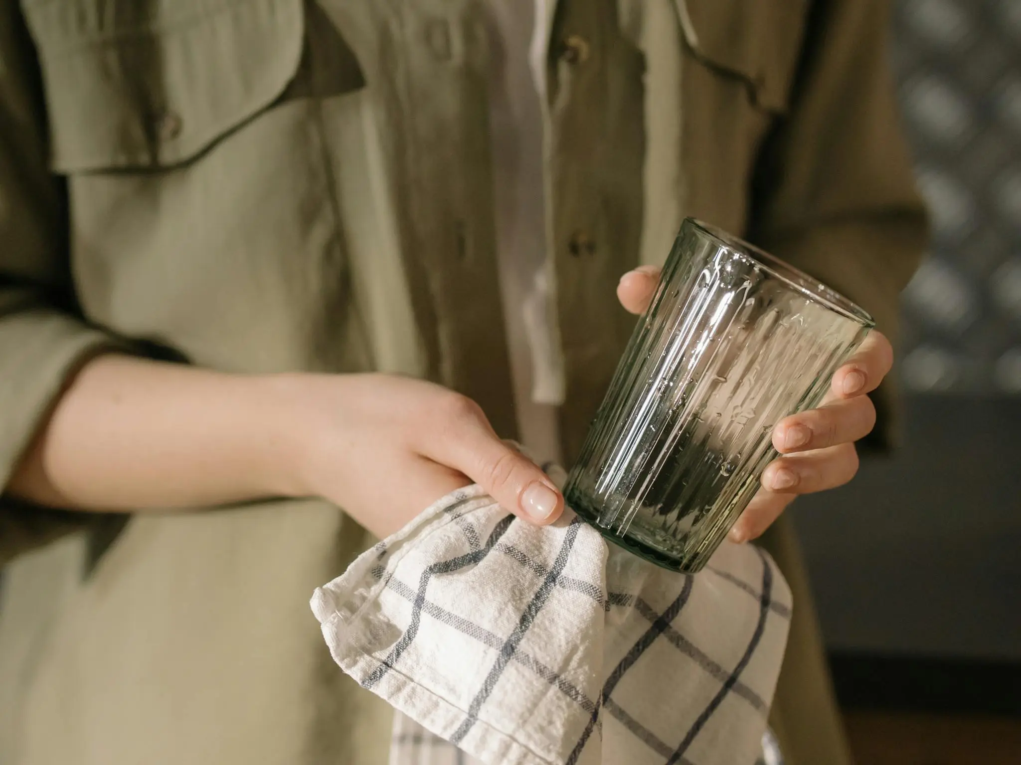 Close-up view of hands drying a glass with a checked cloth in a kitchen setting.